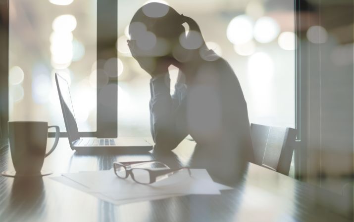 Person sitzt erschöpft am Laptop und hält sich den Kopf als Symbol für Stress und psychische Belastung am Arbeitsplatz